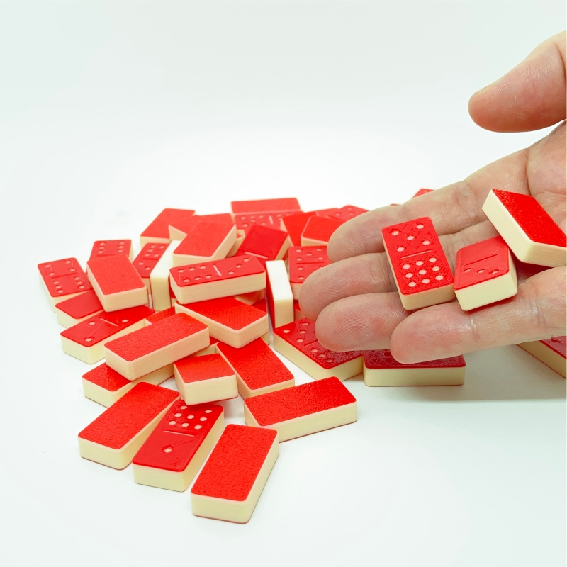 Mini Dominóve SisperDesign, jogo de dominó de 0 a 9 com 55 peças pequenas em vermelho e branco, mostrado sobre fundo branco com uma mão segurando as peças para referência de tamanho.
