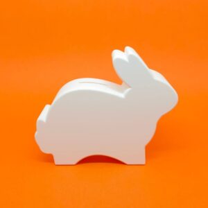 Cofre coelhinho decorativo branco em perfil com fundo laranja.